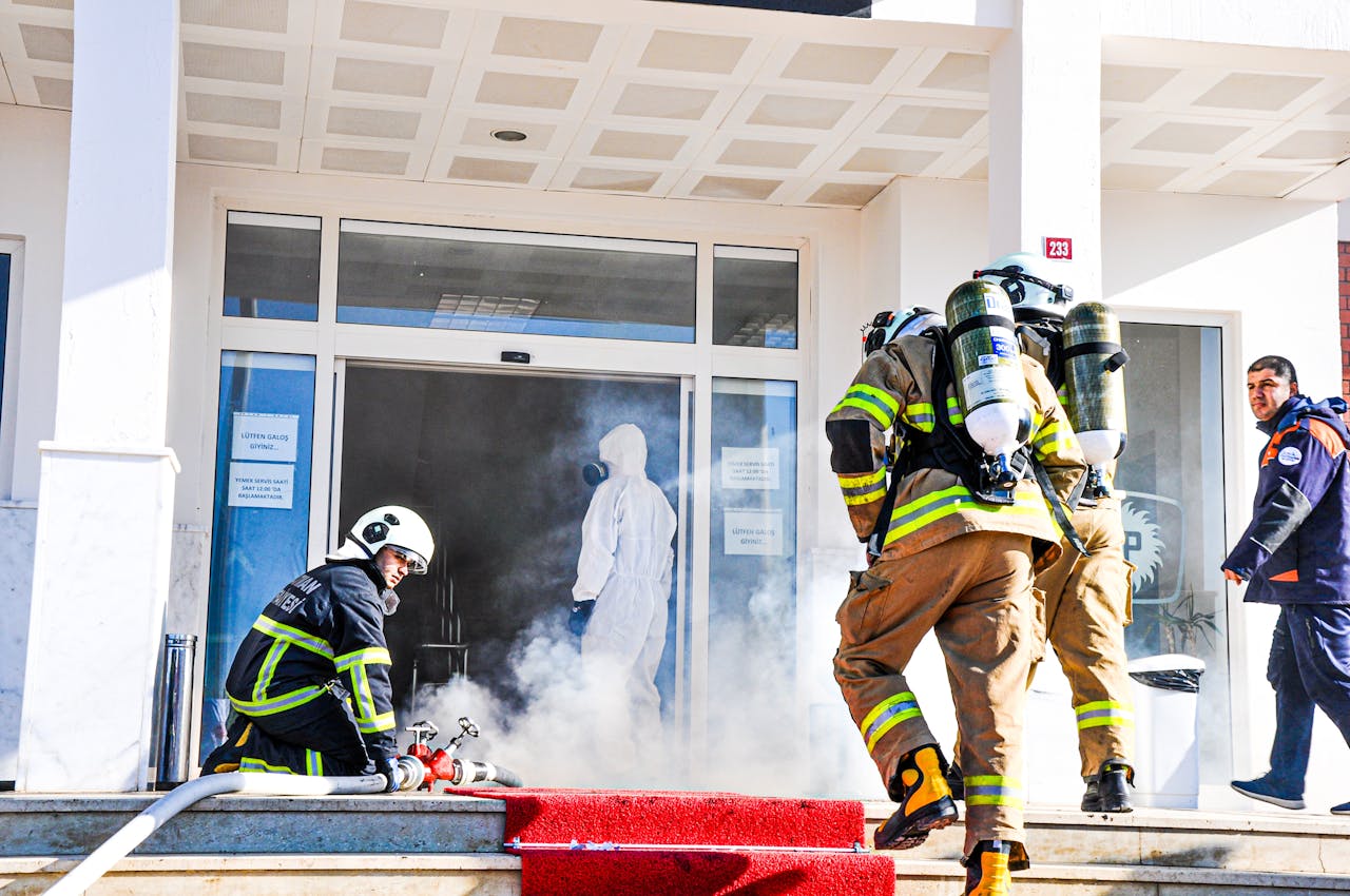 Firefighters responding to an emergency at a building entrance in Batman, Türkiye. Smoke and safety gear visible.